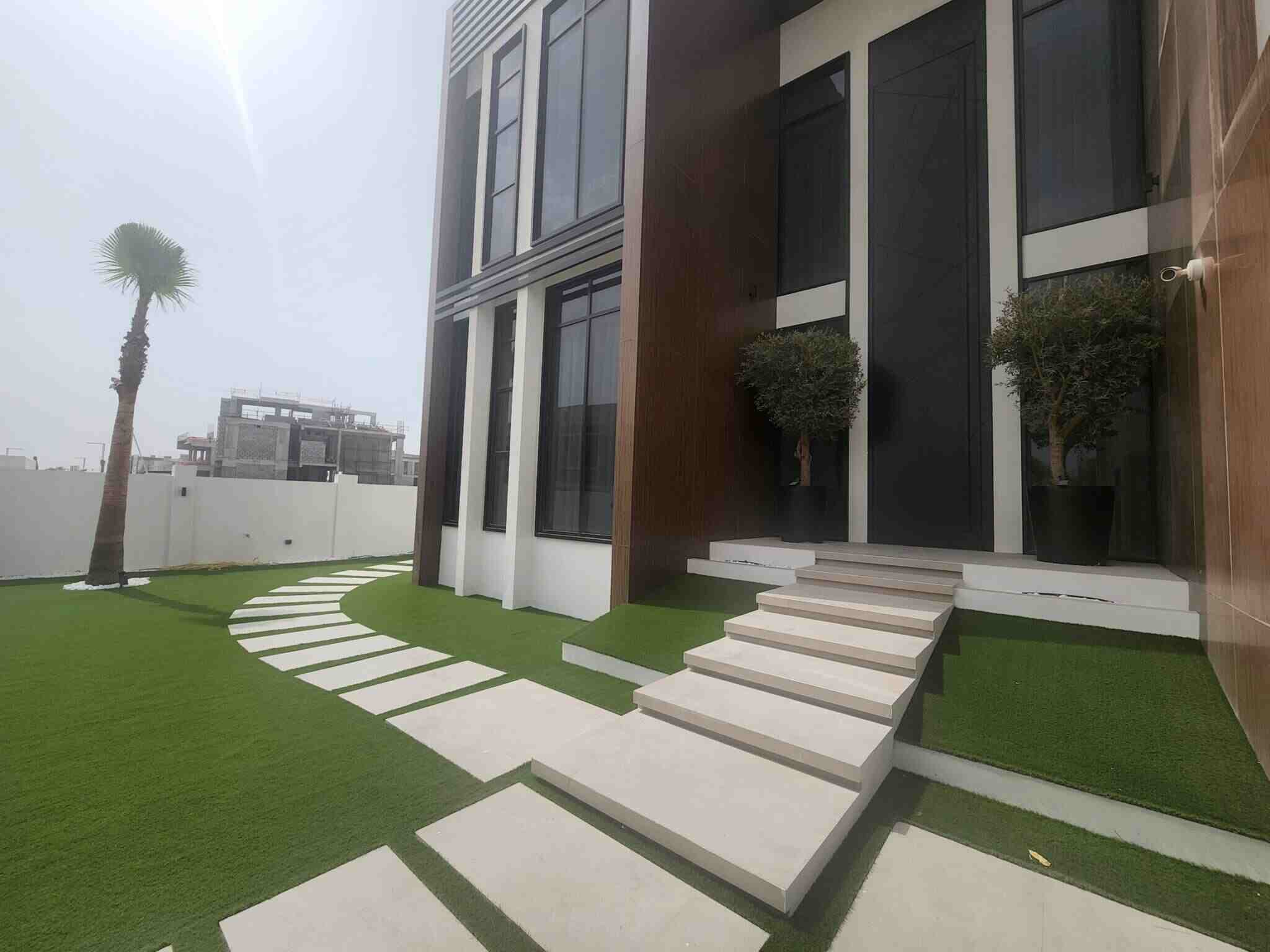 Modern building exterior with large windows, a pathway of stepping stones, and neatly trimmed shrubs